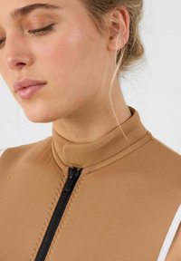 Combinaison de plongée marron à col montant avec une fermeture éclair noire, coutures à plat et rayures blanches sur les épaules. Tissu lisse et extensible.