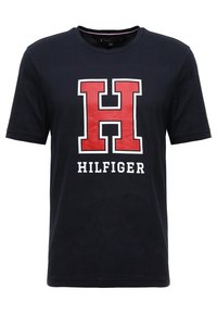 Mörkblå bomullströja med en stor röd "H" och "HILFIGER" i vitt nedanför. Korta ärmar och rund halsringning. Mjuk textur.