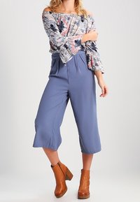 Off-shoulder malli kuvioitu ylhäältä sinisessä, vaaleanpunaisessa ja valkoisessa, yhdistettynä korkeavyötäröisiin sinisiin culotteihin ja ruskeisiin korokepohjaisiin nilkkabootseihin.