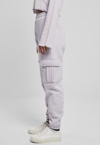 Lawendowe dresy z prążkowanymi akcentami po bokach i kieszeniami, wykonane z miękkiego materiału; elastyczny pas i mankiety, połączone z białymi sneakrsami.