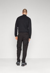 Zwarte lange mouw top met hoge kraag, gecombineerd met zwarte cargobroek met zijzakken en zwarte sportschoenen.