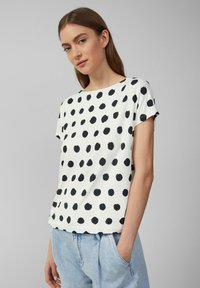 Witte t-shirt met korte mouwen en zwarte stippen, ronde halslijn, zachte stof en een relaxte pasvorm. Gecombineerd met lichtblauwe jeans.
