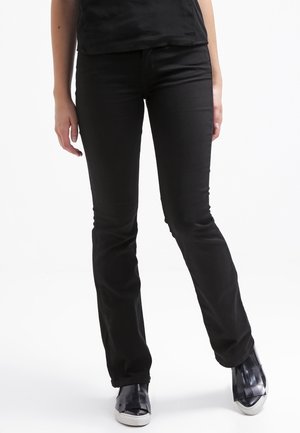 Schwarze Denim-Jeans mit schmaler Passform, Fünf-Taschen-Design und glatter Textur. Kombiniert mit schwarzen Slippern.