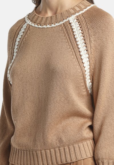 Pulover maro tricotat cu finisaj texturat, având garnitură decorativă albă pe marginea gâtului și pe laterale, tivuri striate și croială lejeră.