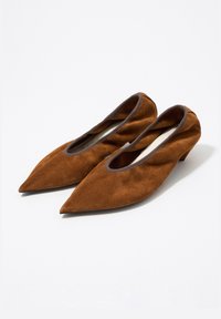 Tacones puntiagudos de ante marrón con un tacón bajo y aberturas elásticas. Presentan un forro interior liso y un ribete oscuro contrastante en los bordes.