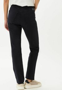 Schwarze gerade geschnittene Hosen mit mittelhoher Taille, Gesäßtaschen und einer glatten Textur. Kombination mit hellen Sneakern.