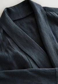 Ciemnoszara lniana szata z wykładanym kołnierzem, o gładkiej fakturze i zwiewnym kroju, z złożonym materiałem wokół dekoltu.