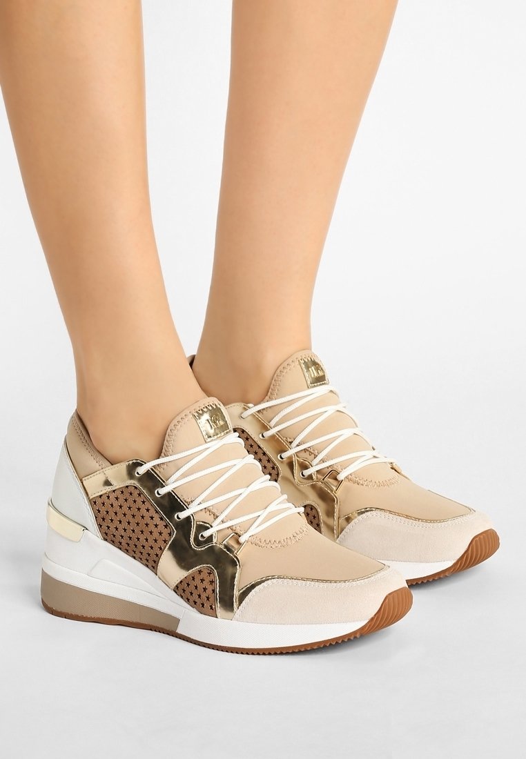 Le scarpe da ginnastica beige presentano accenti in oro metallico, pannelli in rete e lacci bianchi. La suola è texturizzata con un fondo in gomma marrone.