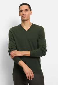 Maglione verde scuro con scollo a V realizzato in un tessuto morbido e dalla trama strutturata. Presenta maniche lunghe con polsini a coste e un design aderente.
