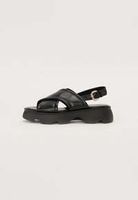 Sorte lærsandaler med kryss-rem design, åpen tå, justerbar ankelrem og chunky plattformsåle med teksturert overflate.