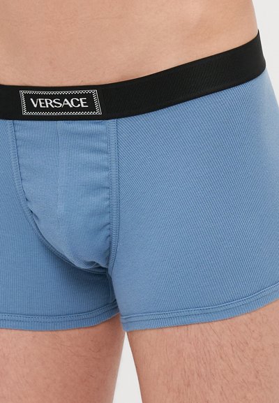 Boxeri scurți cu dungi albastre și o talie elastică neagră ce prezintă un logo alb "VERSACE". Materialul pare neted, cu o textură fină.