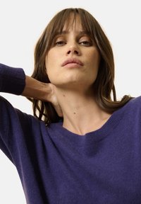 Maglione viola di maglia con scollatura a girocollo e polsini a costine, che mostra una texture morbida e una vestibilità comoda.