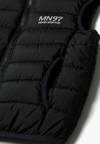 Svart pufferväst med zippered front, kviltat mönster och två sidofickor. Logotypen "MN37 NEVER STOP 97" är tryckt på bröstet.