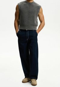 Grå stickad ärmlös tröja med texturerat mönster, ihop med mörkblå vida denimbyxor och beigefärgade slip-on skor.