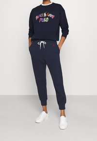 Námořnická mikina s vícebarevným nápisem „PEACE LOVE POLO“, doplněná o odpovídající tepláky. Bílé šňůrky a logo na kalhotách. Bílé tenisky.