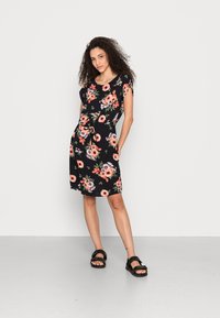 Vestido curto floral em preto com flores laranja e brancas. Mangas curtas, cintura ajustável, até aos joelhos. Usado com sandálias pretas.