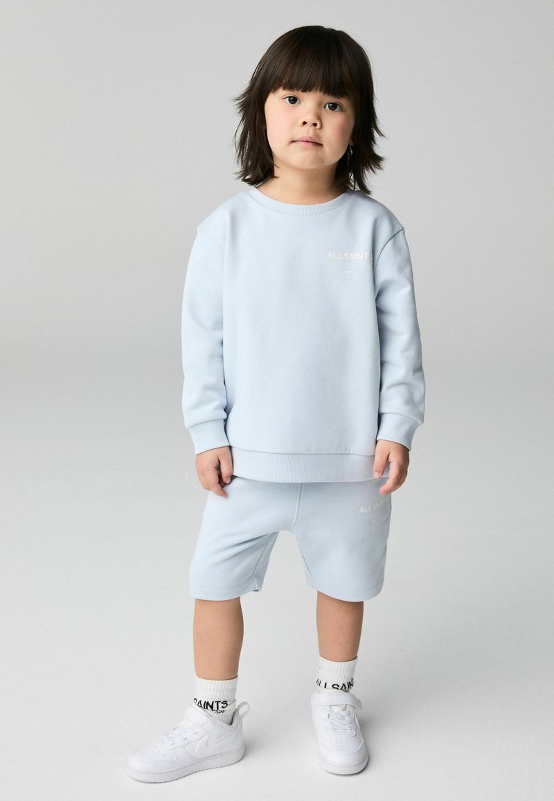 Conjunto de sudadera y pantalones cortos de color azul claro, hecho de algodón suave, con un logo minimalista. Combinado con zapatillas blancas y calcetines de canalé.