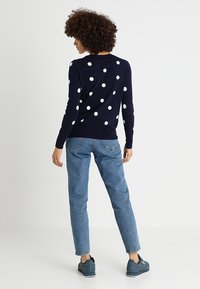 Granatowy sweter z dużymi białymi kropkami, z prążkowanymi mankietami i dołem, w połączeniu z jasnoniebieskimi dżinsami i ciemnymi trampkami.