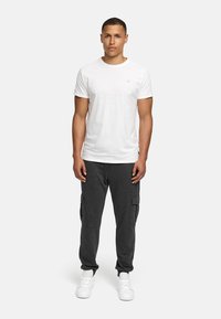 White cotton t-shirt with short sleeves, paired with dark gray cargo pants featuring side pockets. Model wears white sneakers.