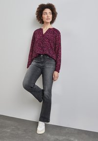 Blus med blommönster i fuchsia och svart, kombinerad med mörkgrå utsvängda jeans och vita sneakers, vilket ger en avslappnad outfit.