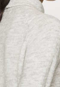 Pull gris clair avec un col côtelé, fabriqué en tissu doux et texturé. Présente une coupe ajustée et un motif subtil sur toute la surface.