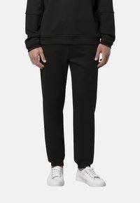 Pantaloni della tuta neri realizzati in tessuto morbido con polsini elasticizzati. Abbinati a sneakers bianche, con un design semplice e moderno.