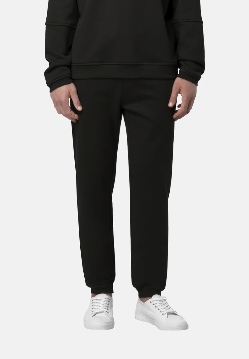 Pantaloni della tuta neri realizzati in tessuto morbido con polsini elasticizzati. Abbinati a sneakers bianche, con un design semplice e moderno.