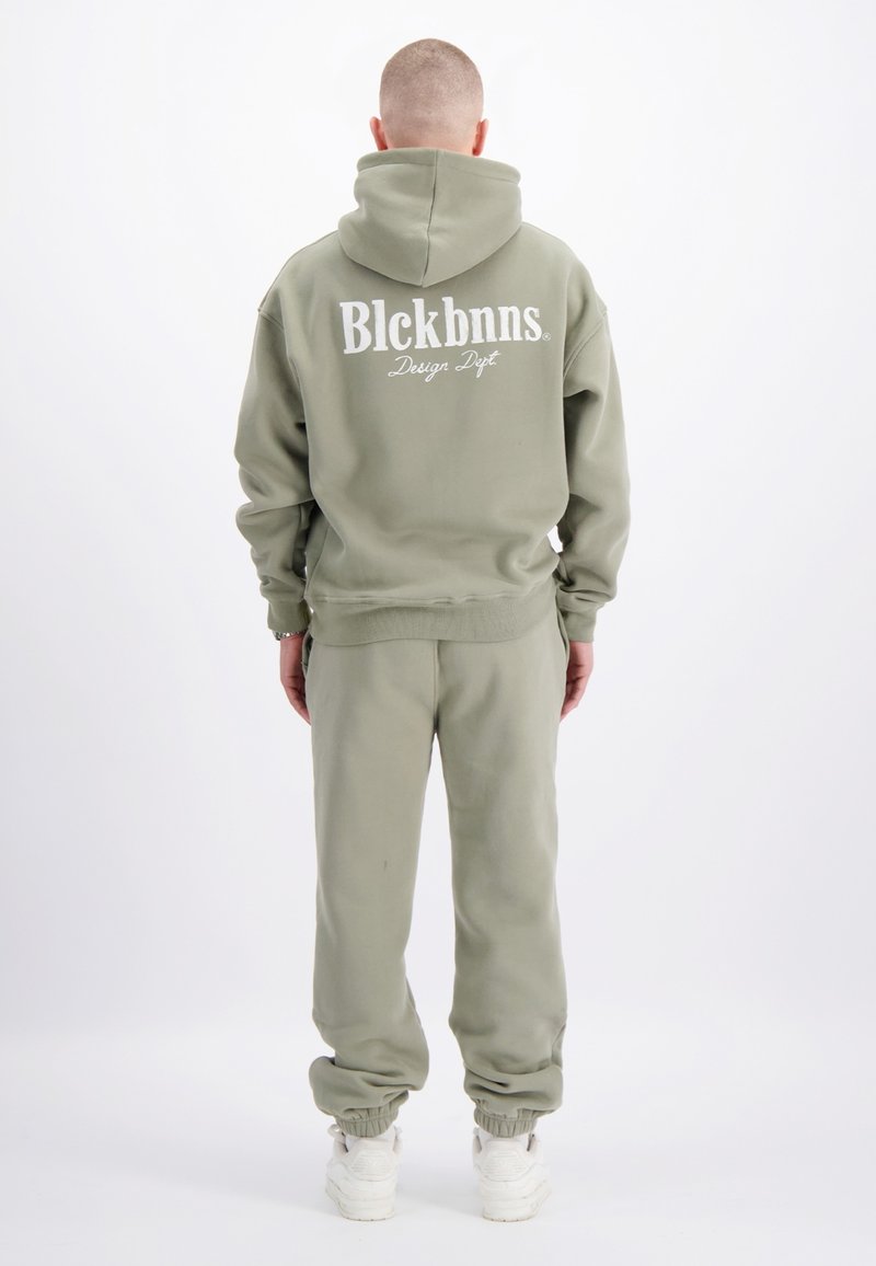 Olijfgroene hoodie en joggingbroek set. Hoodie heeft een groot wit logo op de achterkant, geribbelde manchetten en een kangoeroezak. Gladde textuur, comfortabele pasvorm.