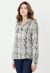 Koszula z długim rękawem w wzór węża, utrzymana w jasnobeżowej, czarnej i szarej kolorystyce, z kołnierzykiem i zapięciem na guziki.