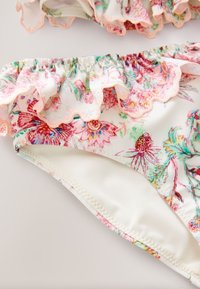 Slip de bikini cu imprimeu floral, margini tivite cu volănașe în culori pastelate, cu captuseală interioară albă și detalii fine de cusături roz.