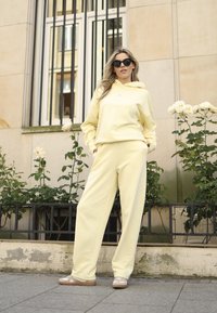 Geel hoodie met een voorzak en bijpassende sweatpants; gladde textuur en relaxte pasvorm; gecombineerd met lichtbruine schoenen.