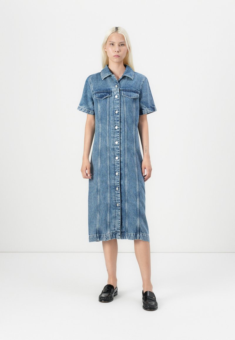 Abito in denim con colletto, maniche corte, chiusura frontale con bottoni, due tasche sul petto e orlo di lunghezza media.