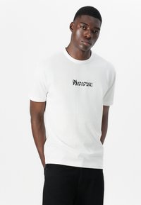 White cotton t-shirt featuring a textured black graphic print centered on the front. Short sleeves and a crew neck design.