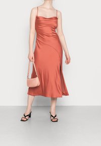 Saténové midi šaty v barvě prachově růžové, s korálkovým výstřihem, tenkými ramínky, asymetrickým designem a bočním rozšířením. Vypadají skvěle v kombinaci s černými sandály na podpatku a malou růžovou kabelkou.