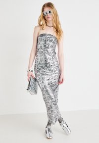 Metallihopea ilman hihnoja oleva mekko, jossa on käärmeennahkakuosi, slim fit. Yhdistetty hopeisten asusteiden ja aurinkolasien kanssa neutraalilla taustalla.