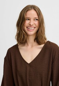 Haut marron texturé à col en V avec des manches amples, présentant un motif en tissu froissé et une coupe décontractée.