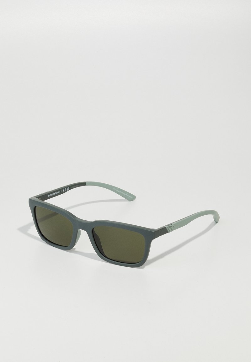 Ochelari de soare rectangulari cu lentile de culoare verde închis. Ramele sunt de culoare gri mat, cu o textură netedă. Brațele au un logo subtil și o culoare contrastantă.