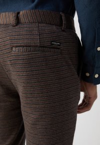Brown and navy patterned trousers made from textured fabric with a back pocket and a Scotch & Soda label. Features a fitted design.