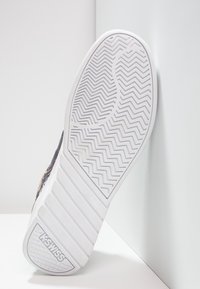 Semelle de basket blanche avec un motif de bande de roulement en zigzag, dotée d'un caoutchouc texturé. Logo de la marque "KSWISS" embossé près du talon.