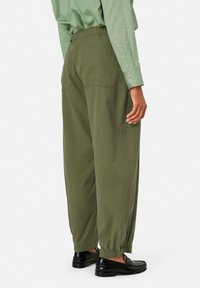 Groene elastische taillebroek met twee achterzakken, geplooide manchetten en een ontspannen pasvorm. Gecombineerd met zwarte instappers.