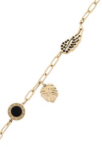 Collana in oro con charm, tra cui un disco circolare nero con numeri romani, una foglia di monstera e un'ala con pietre nere.
