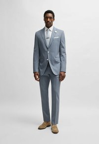 Light gray tailored suit featuring a single-breasted jacket with notched lapels, paired with matching slim-fit trousers and beige shoes.