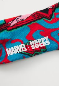Krāsainas zeķes ar izteiksmīgu zilu un sarkanu rakstu, ar teksturētu audumu un baltu zīmolu, kas lasāms "MARVEL | HAPPY SOCKS."