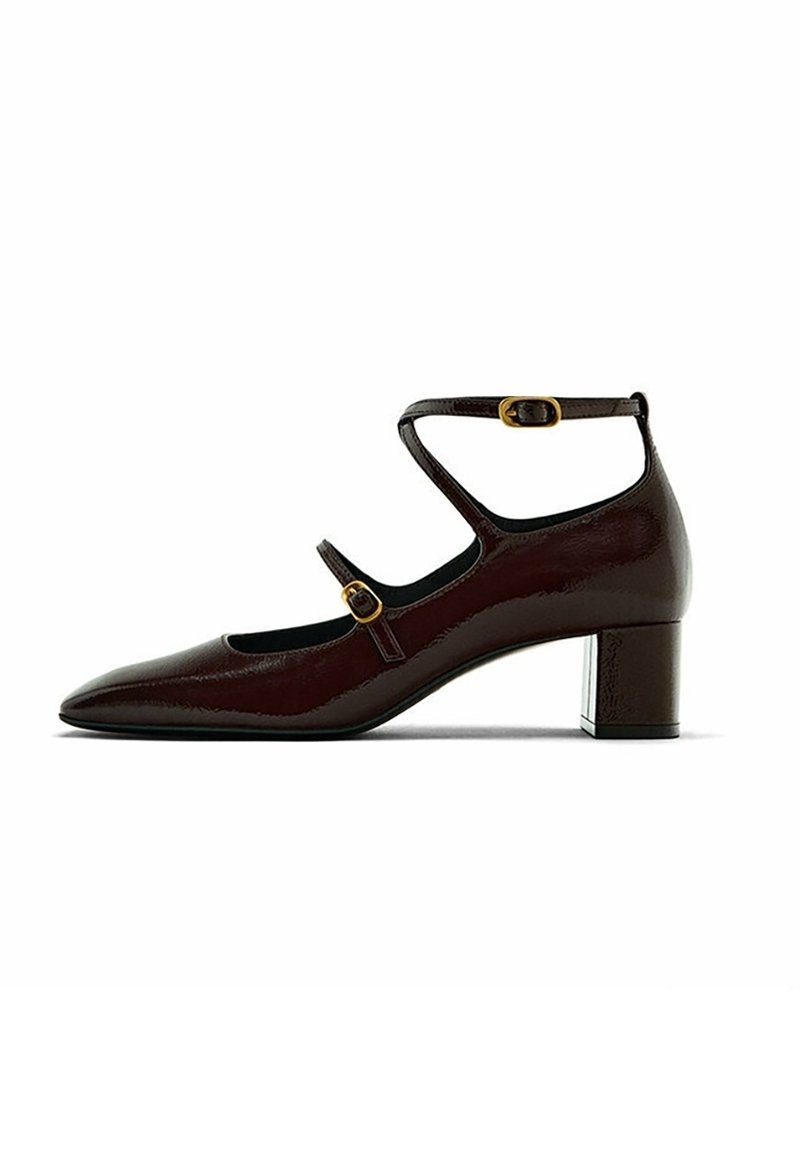 Chaussure en cuir verni bordeaux foncé avec un bout pointu, une bride à la cheville, une boucle en métal doré et un petit talon carré. Texture lisse, design élégant.