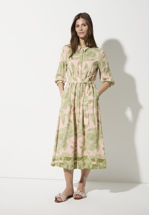 Robe midi florale en rose et vert, en mélange de coton, col, devant à boutons, poignets élastiques, ceinture à la taille, poches latérales. Associée à des sandales à enfiler nouées.