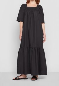Robe maxi noire avec un décolleté carré, des manches courtes bouffantes et un ourlet à volants froncé. Tissu lisse avec une silhouette simple et décontractée.
