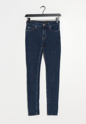 Jeans skinny de mezclilla azul oscuro con una cintura de altura media, cinco bolsillos, costuras naranjas y un cierre de botón estándar.