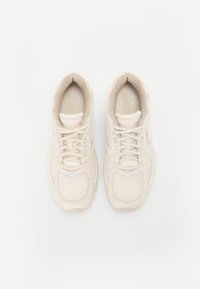 Baskets de sport beiges avec des panneaux en maille, bout rond et lacets plats. Présente un logo discret et une semelle texturée pour une meilleure adhérence.