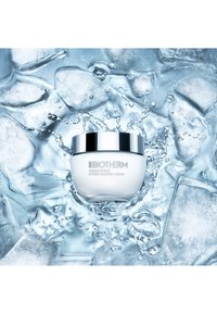 Biotherm Aquasource Hydra Barrier Cream in een witte pot met een zilveren deksel, omringd door ijsblokjes en spetterende waterdruppels.