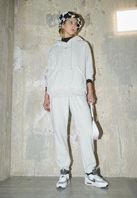 Vaaleanharmaa huppari ja housut, jotka on valmistettu fleecestä, yhdistetty valkoisiin ja harmaisiin tennareihin sekä mustavalkoiseen kuvioituun metsätakkiin.